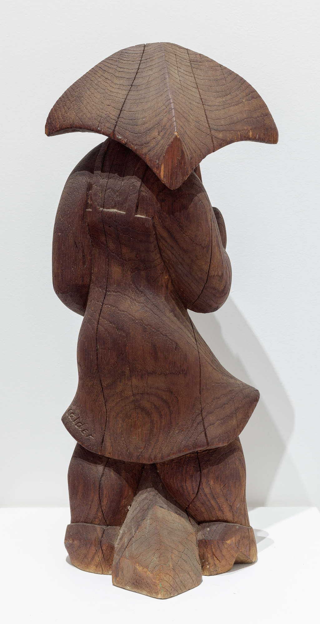After disappointing sales at Weyhe Gallery in 1928, Calder turned from sculpted wire portraits and figures to the more conventional medium of wood. On the advice of sculptor Chaim Gross, he purchased small blocks of wood from Monteath, a Brooklyn supplier of tropical woods. He spent much of that summer on a Peekskill, New York farm carving. In each case, the woodblock suggested how he might preserve its overall shape and character as he subsumed those attributes in a single form.  There was a directness about working in wood that appealed to him. Carved from a single block of wood, Woman with Square Umbrella is not very different from the subjects of his wire sculptures except that he supplanted the ethereal nature of using wire with a more corporeal medium.
<br>© 2023 Calder Foundation, New York / Artists Rights Society (ARS), New York